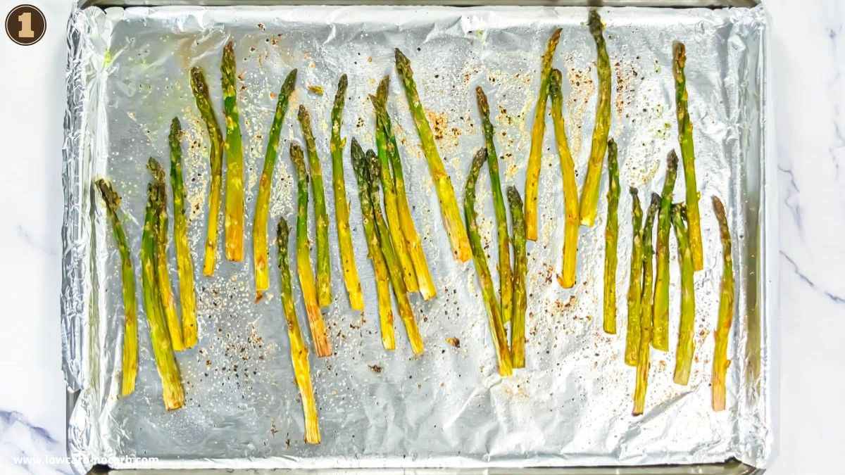 Roasted asparagus spears arranged on a foil-lined baking sheet, seasoned with herbs and spices.
