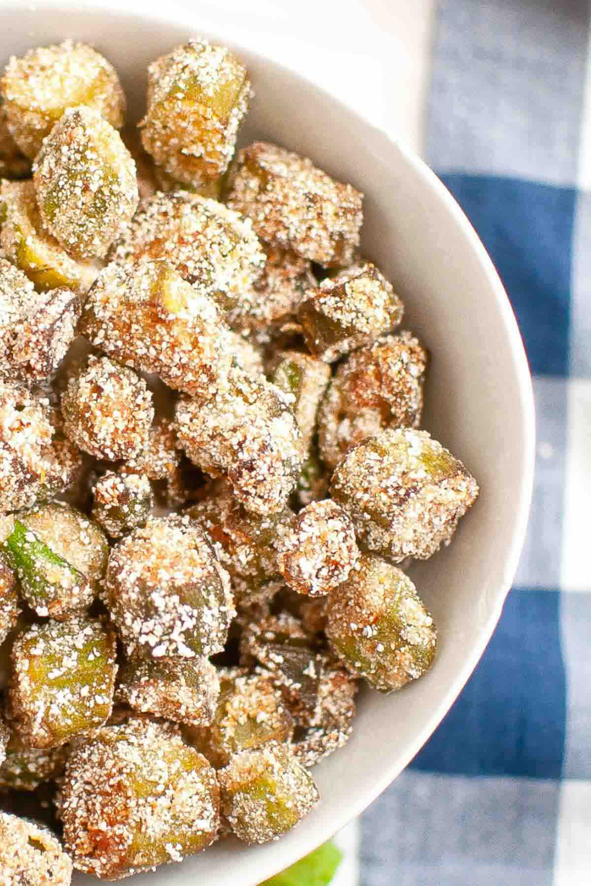 A white bowl filled with crispy, breaded fried okra pieces, shown from above on a blue and white checkered cloth.
