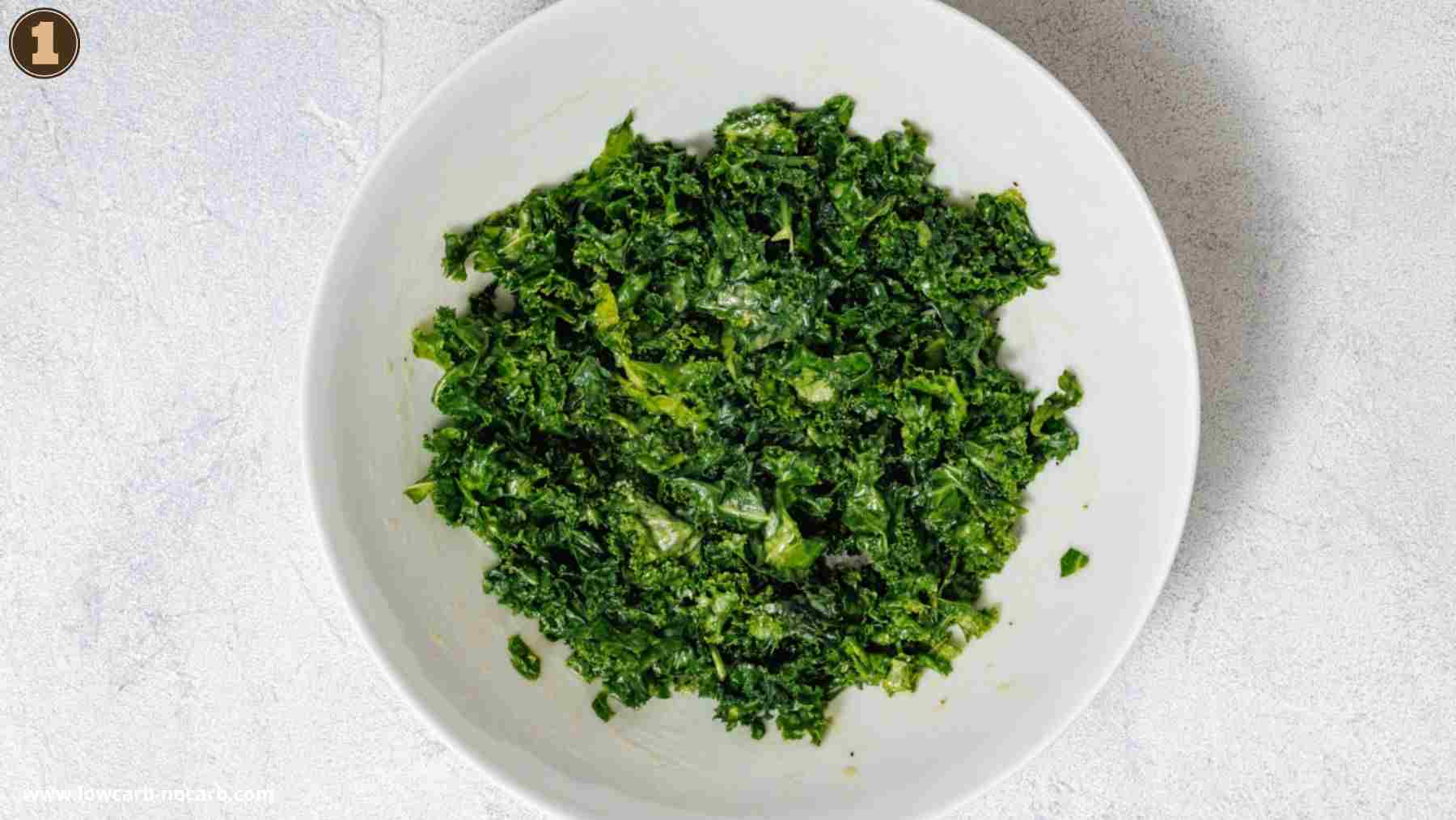 A white bowl filled with chopped, massaged kale sits on a light-colored surface.