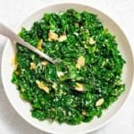 A white bowl filled with chopped kale salad topped with sliced almonds, grated cheese, and a spoon resting inside.