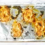 Four cooked pork chops with seasoning on a foil-lined baking sheet, with juices and browned spots visible.