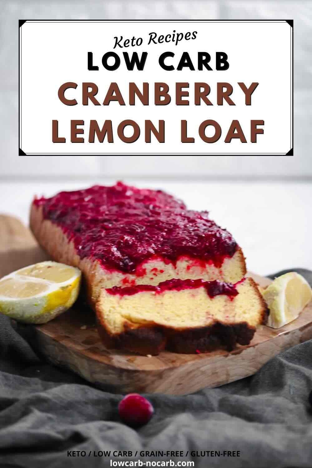 A sliced loaf of cranberry lemon bread with cranberry topping sits on a wooden board, garnished with lemon halves and a cranberry, against a blurred background.
