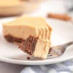 A fork holds a bite of creamy pie with a chocolate crust, with the rest of the pie slice on a white plate in the background.