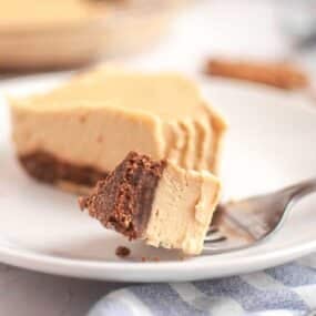 A fork holds a bite of creamy pie with a chocolate crust, with the rest of the pie slice on a white plate in the background.