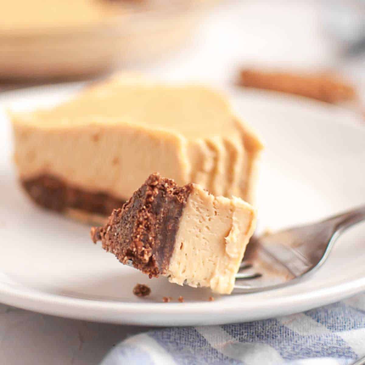 A fork holds a bite of creamy pie with a chocolate crust, with the rest of the pie slice on a white plate in the background.