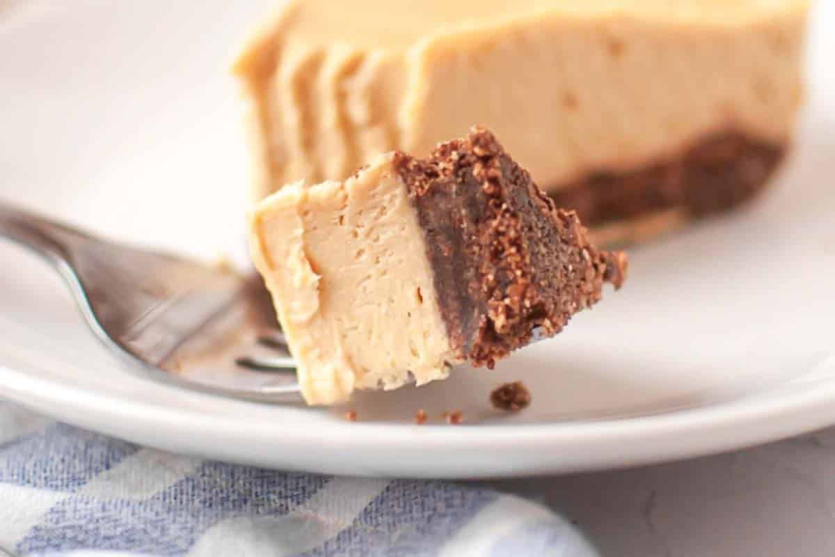 A fork holds a bite of creamy dessert with a chocolate base, in front of a partially eaten slice on a white plate.