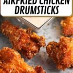 Four crispy air-fried chicken drumsticks on a tray with a square bowl of dipping sauce in the background.