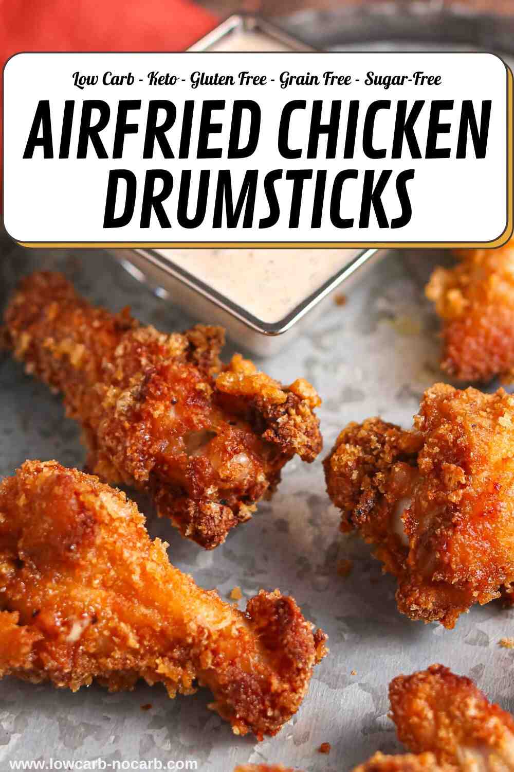 Four crispy air-fried chicken drumsticks on a tray with a square bowl of dipping sauce in the background.