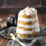 Layered pumpkin dessert in a glass topped with whipped cream and cinnamon.