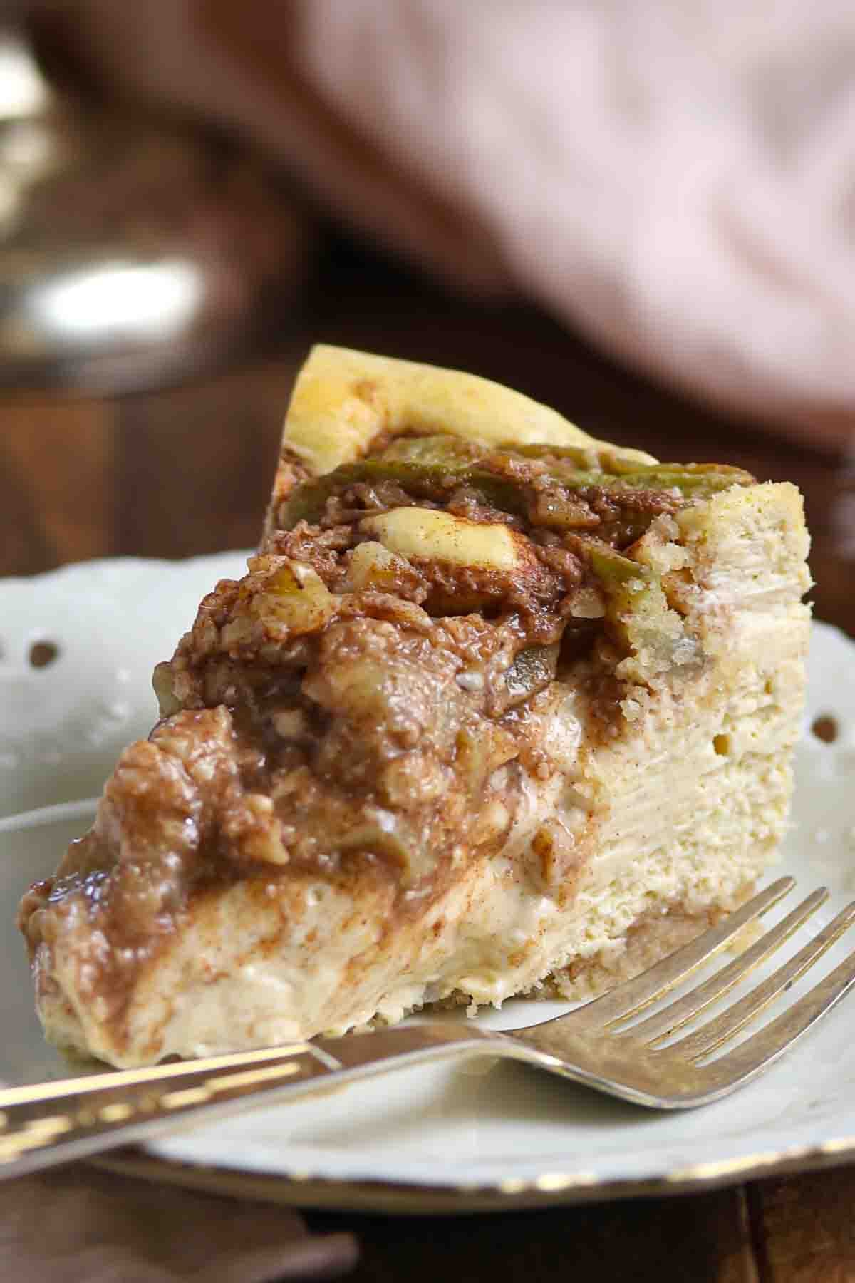 A slice of apple streusel cheesecake on a plate with a fork.