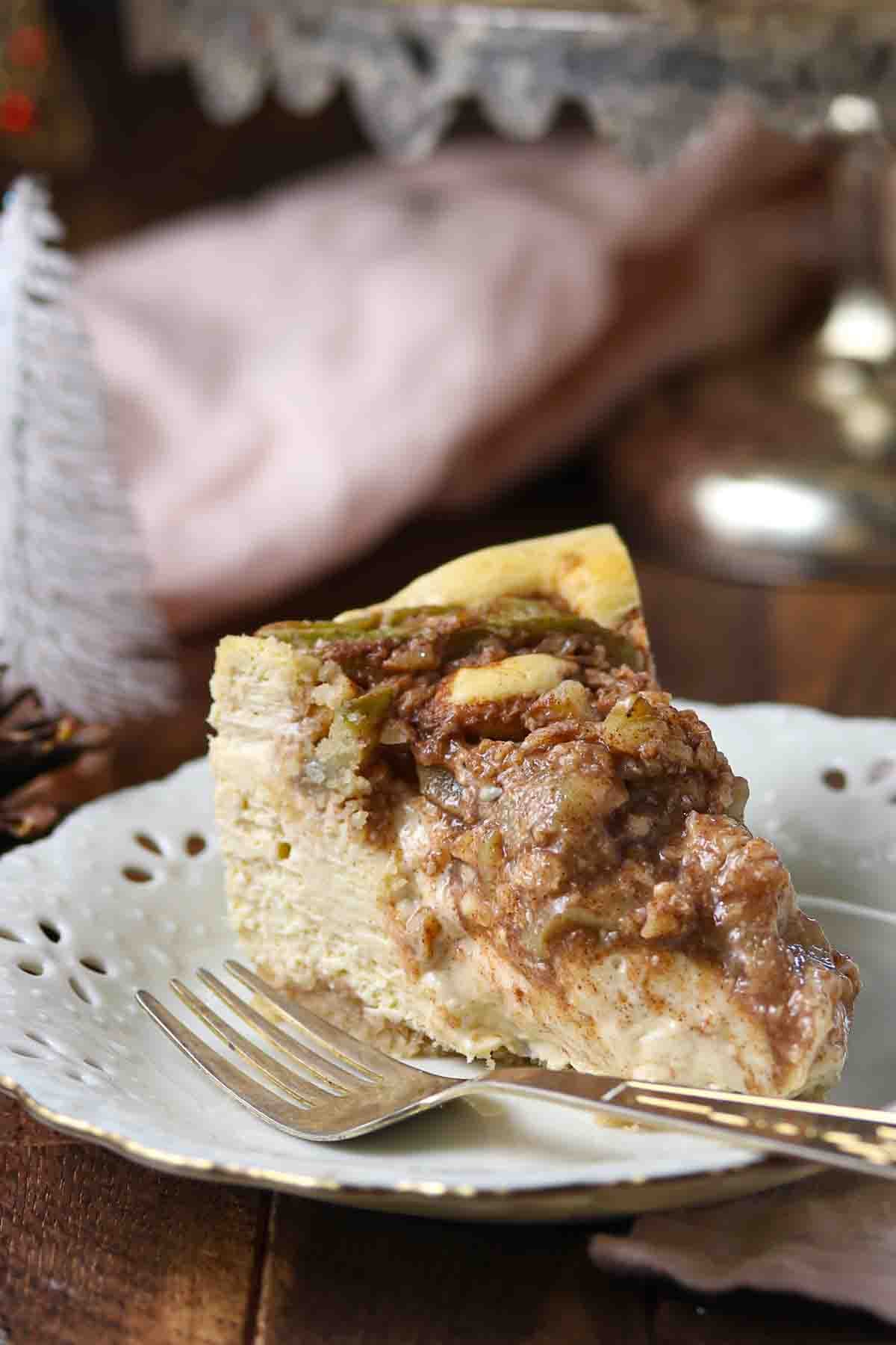 A slice of apple cheesecake on a decorative white plate with a fork.