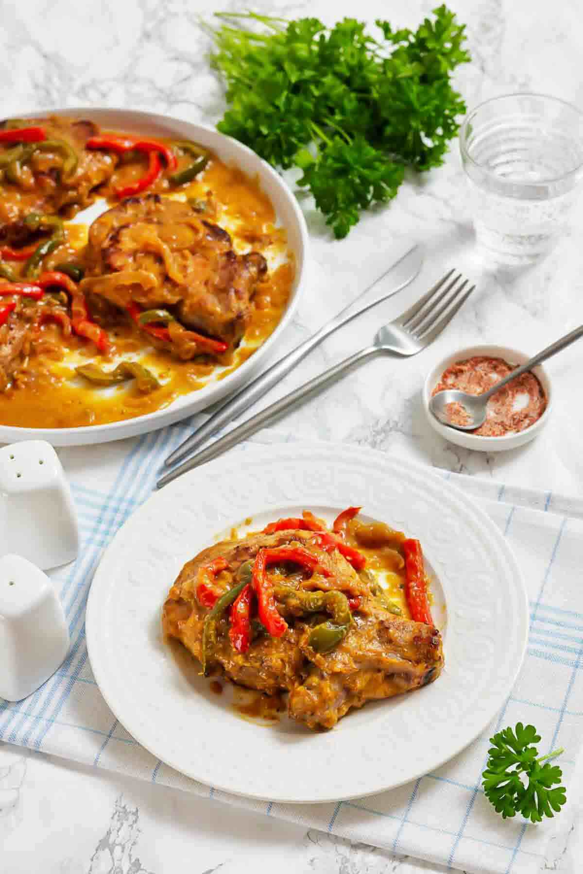 Pork chops with sautéed peppers and onions in a creamy sauce, served on a white plate.