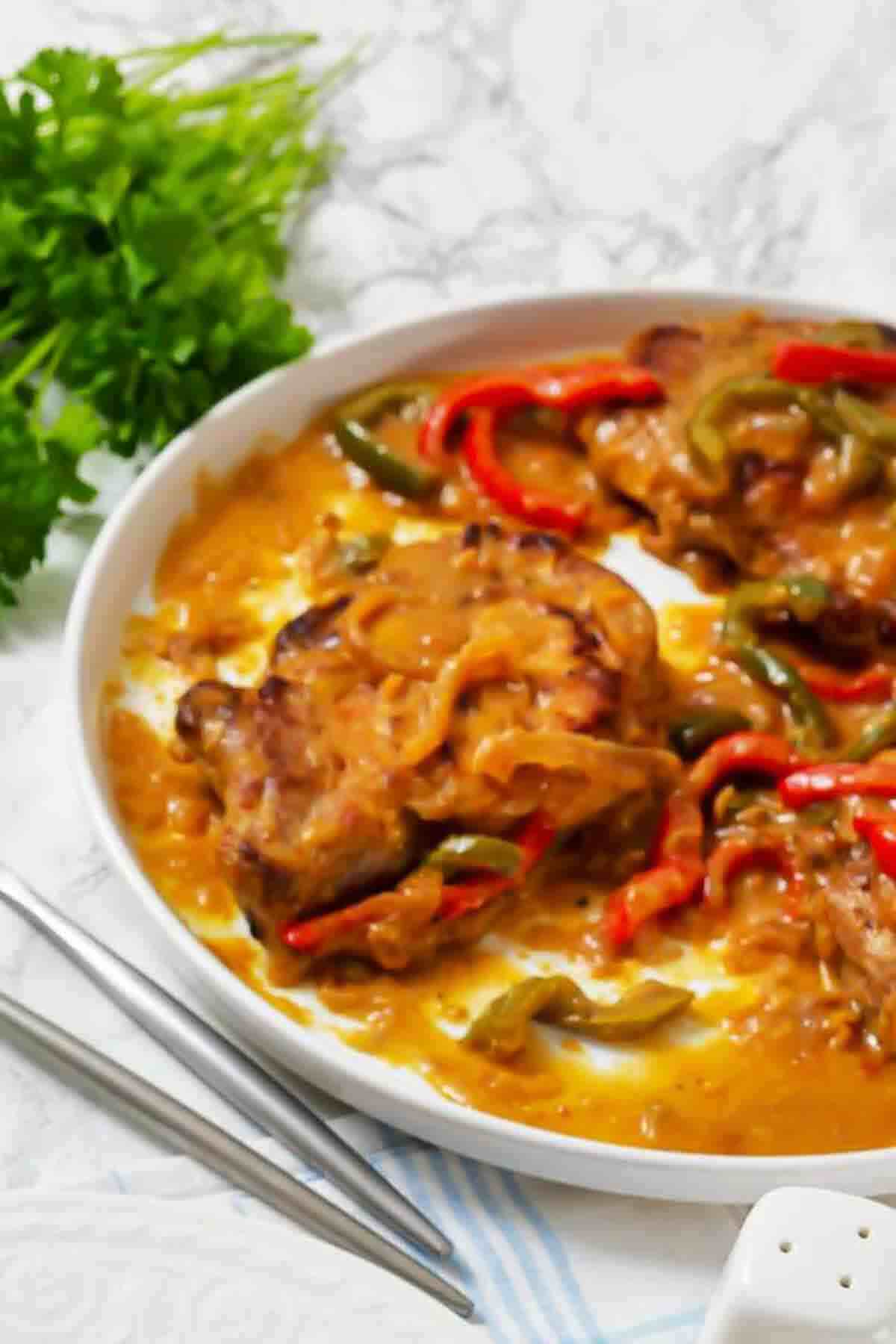 Pork chops smothered in a creamy sauce with red and green bell pepper strips on a white plate.